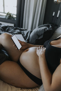 Pregnant woman relaxing in bed and using pregnancy app on phone