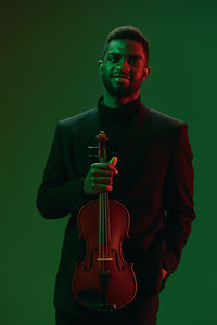 Portrait of young man holding violin against blue background