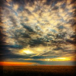 Scenic view of landscape against cloudy sky at sunset