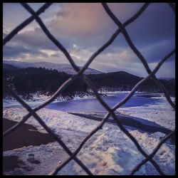 Snow covered chainlink fence against sky during winter