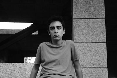 Portrait of young man sitting against wall