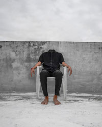 Rear view of man sitting on wall against sky