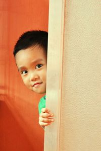 Portrait of cute boy hiding behind wall