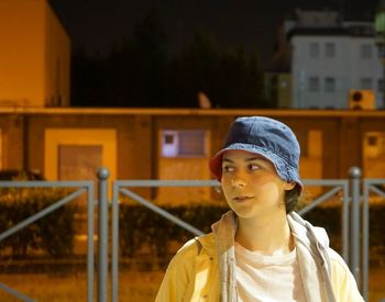 Portrait of young woman looking away against building