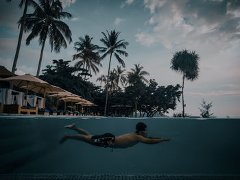 Side view of shirtless man swimming in pool against sky