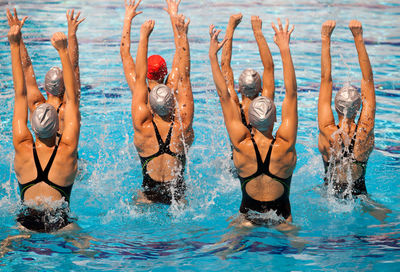 Rear view of people with arms raised in swimming pool during competition