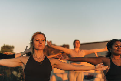 Woman with arms outstretched exercising with female friend at sunset