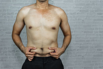 Midsection of shirtless man standing against wall