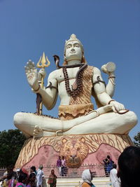 Low angle view of people visiting shiva statue against clear blue sky