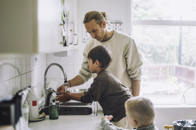 Male teacher guiding boys to wash hands near sink at child care center