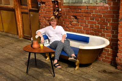 Full length portrait of woman sitting on seat against wall