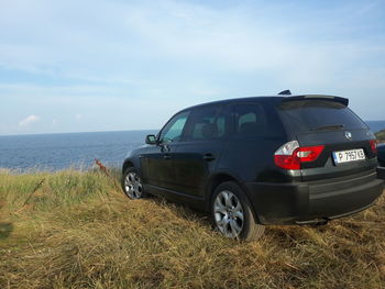 Vintage car on field by sea against sky