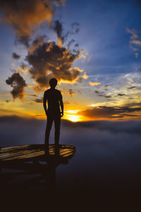 Rear view of man standing at beach against sky during sunset