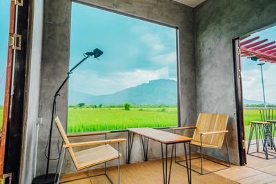 Empty chairs and tables against sky seen through window