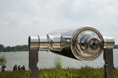 Close-up of coin-operated binoculars on field against sky