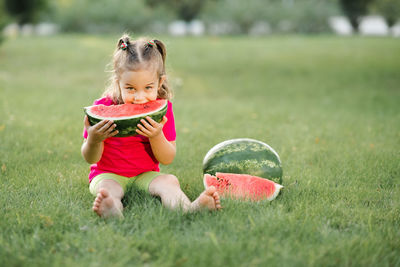 Funny cute child girl 3-4 year old eating ripe watermelon on green grass outdoor. 