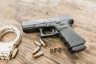 High angle view of handgun with bullets and handcuffs on wooden table