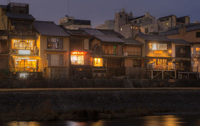 Illuminated buildings by river against sky at night