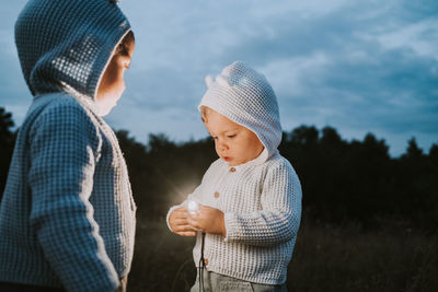 Baby boy holding illuminated light while standing with brother on field