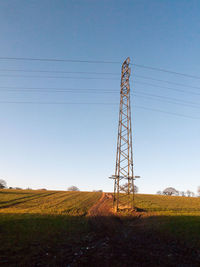 Low angle view of electricity pylon on field against clear sky