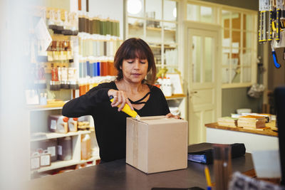 Mature female owner opening cardboard box at checkout counter in furniture store