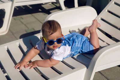 Child in a denim suit and sunglasses lying on a plastic chaise longue