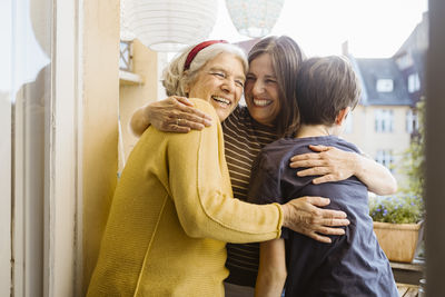 Happy woman embracing mother-in-law and son while standing in balcony