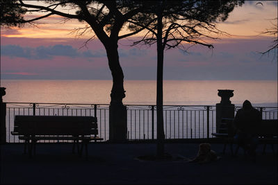 Silhouette people sitting on bench by sea against sky during sunset