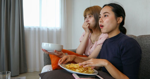 Young women watching tv while sitting with food on table