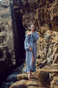 Fashionable brunette woman in a gray dress stands on a cheese rock in the summer