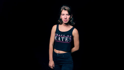 Portrait of young woman standing against black background