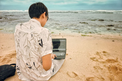 Rear view of man using mobile phone at beach