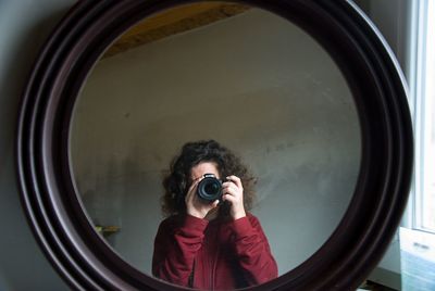 Portrait of woman photographing with camera seen on mirror