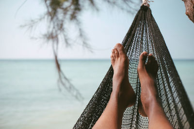 Low section of woman on hammock at beach against sky