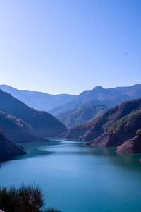 Scenic view of lake and mountains against clear blue sky