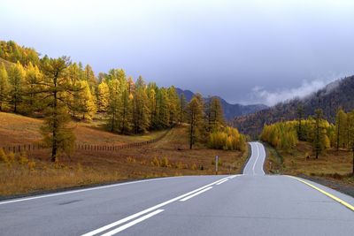 Country road amidst trees against sky