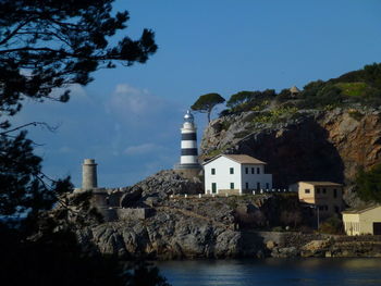 Buildings and lighthouse by trees against sky 