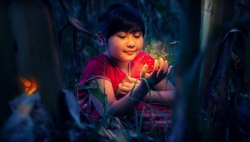 Close-up of girl playing with fireflies on grassy field at night