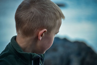 Close-up of boy looking away against sky