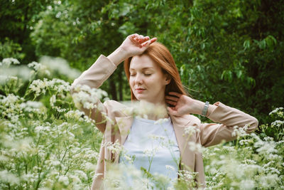 Young woman with arms raised standing against plants