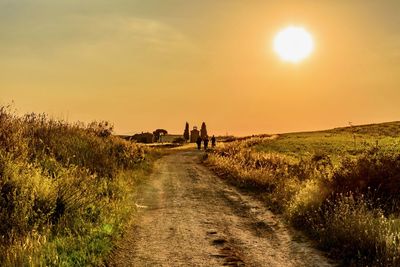 Dirt road amidst grassy field against sky during sunset