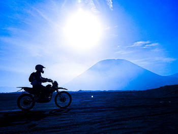 Side view of man riding motorcycle on land against sky during sunset