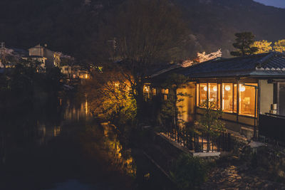 Illuminated buildings by river against sky at night