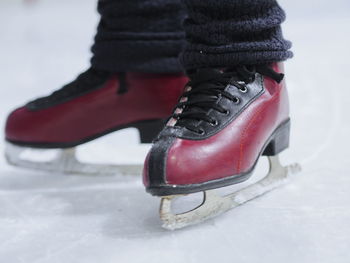 Low section of person wearing ice skate while standing on snow