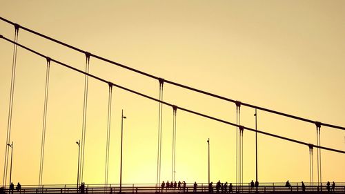 Low angle view of silhouette people on bridge against clear orange sky