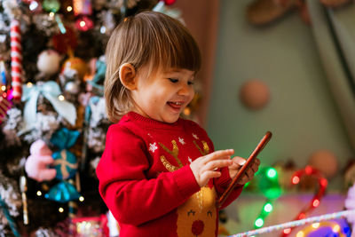 Happy little girl in a red sweater, joyfully holding the phone, near