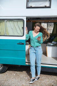 Woman using mobile phone at entrance of camper van
