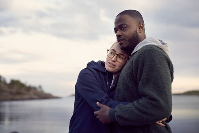 Couple standing at beach against sky during sunset