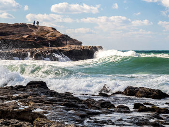 Waves splashing on rocks against sky