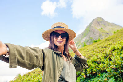 Portrait of young woman wearing hat standing against sky